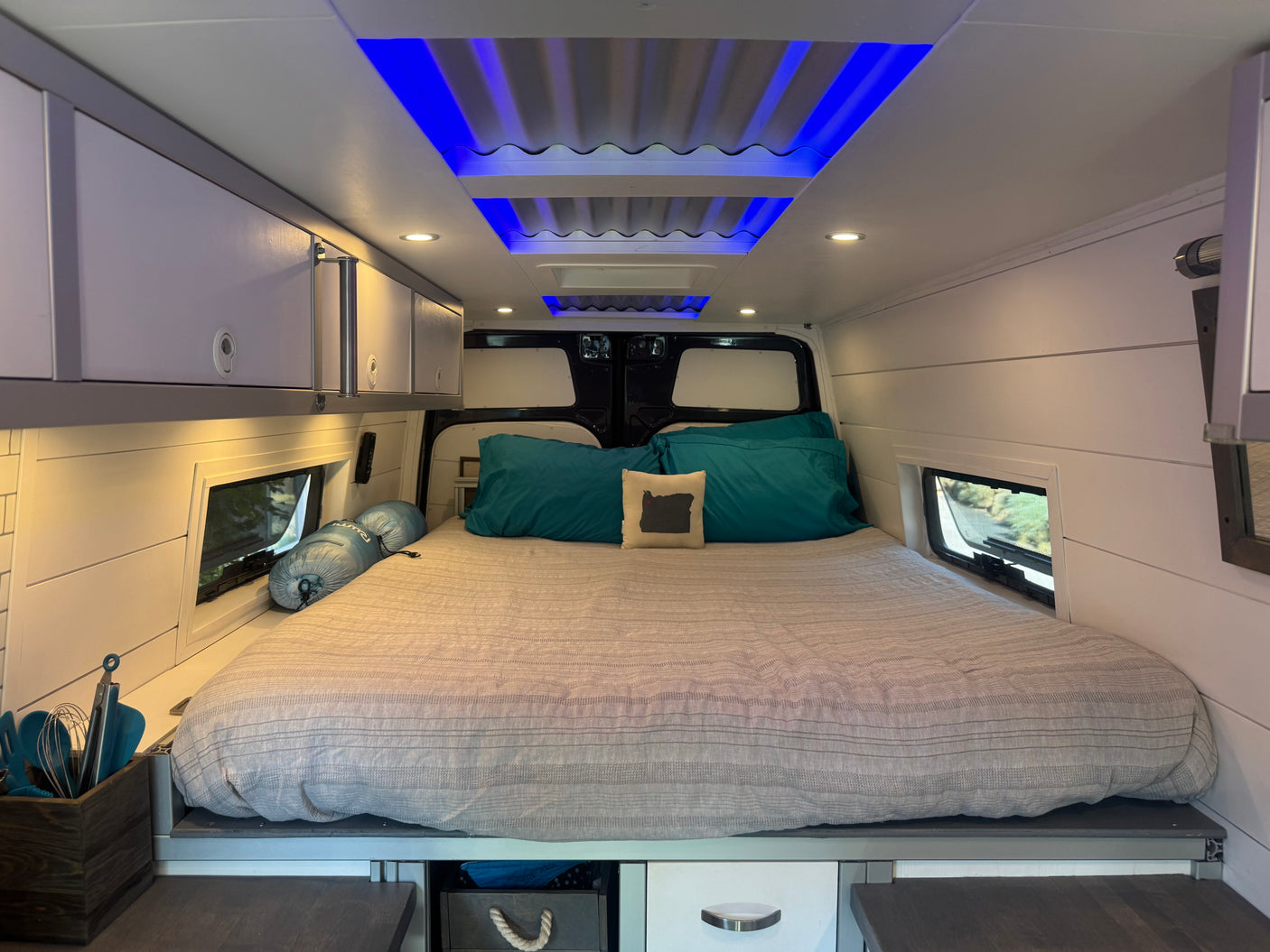 Modern RV rental interior with a comfy bed, sleek storage, ambient blue lighting, and practical windows.