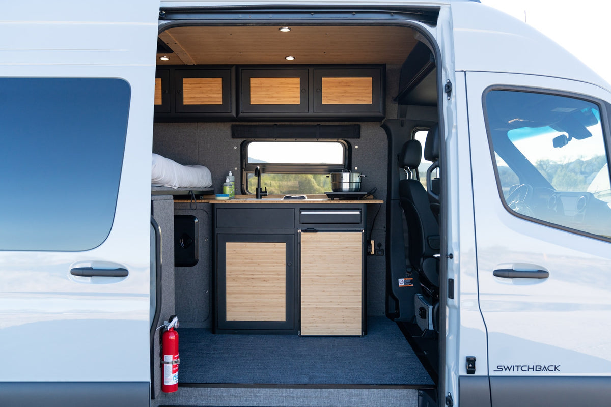 View inside an rv rental camper van, revealing its modern interior with a compact kitchen, bed, and bamboo cabinets. — photo 8
