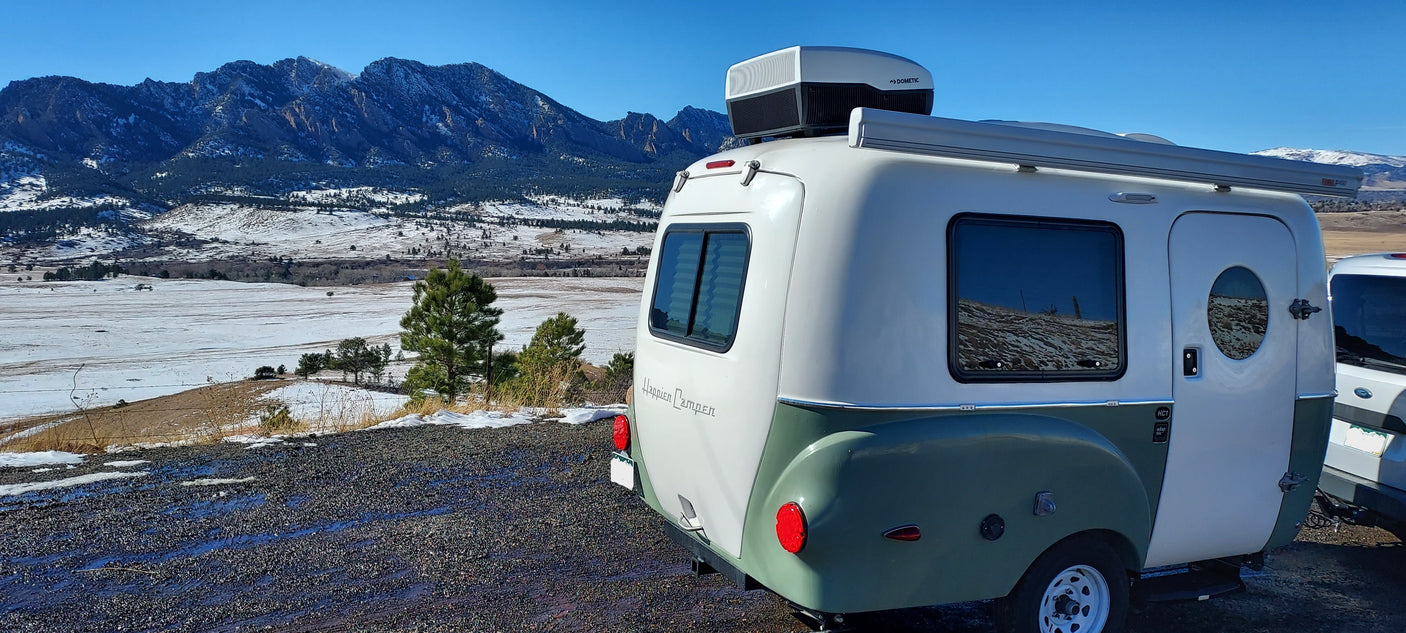 This white and green Happier Camper RV rental sits on a scenic overlook with snow-dusted mountains and valley in winter.