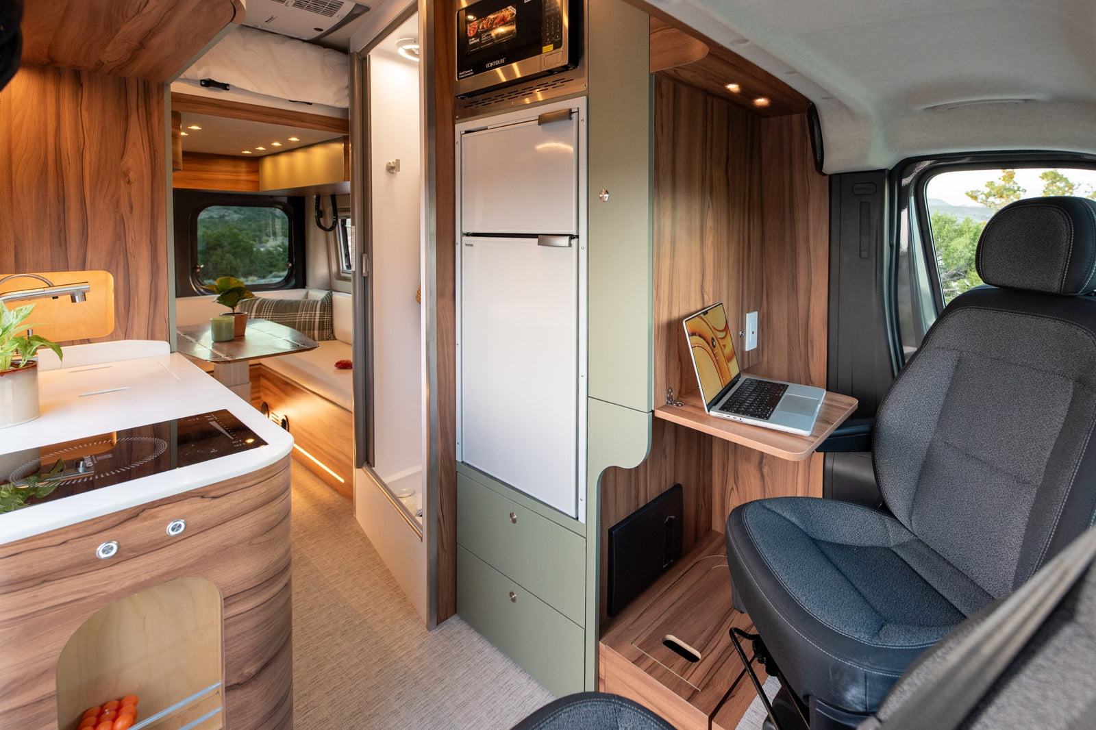 Modern rv rental interior with a kitchen, refrigerator, microwave, laptop workstation, and dining area.