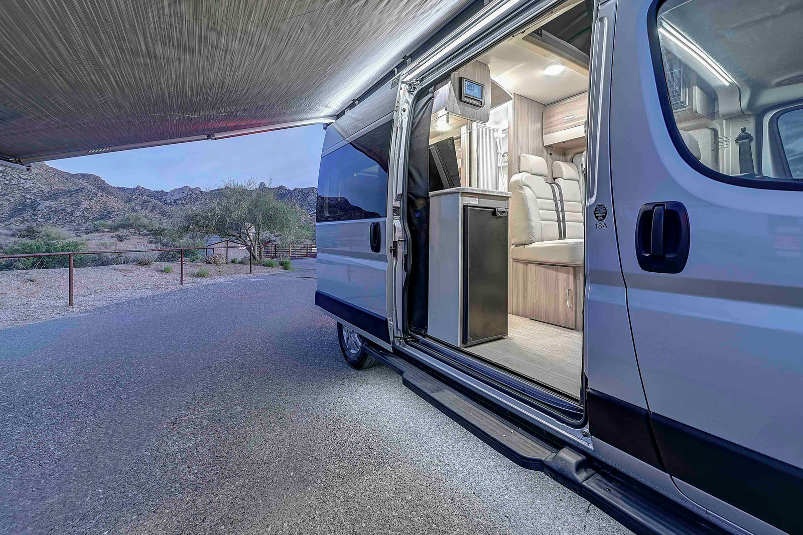 RV rental with an open door and extended awning, showcasing its interior lights against a mountain backdrop at dusk.