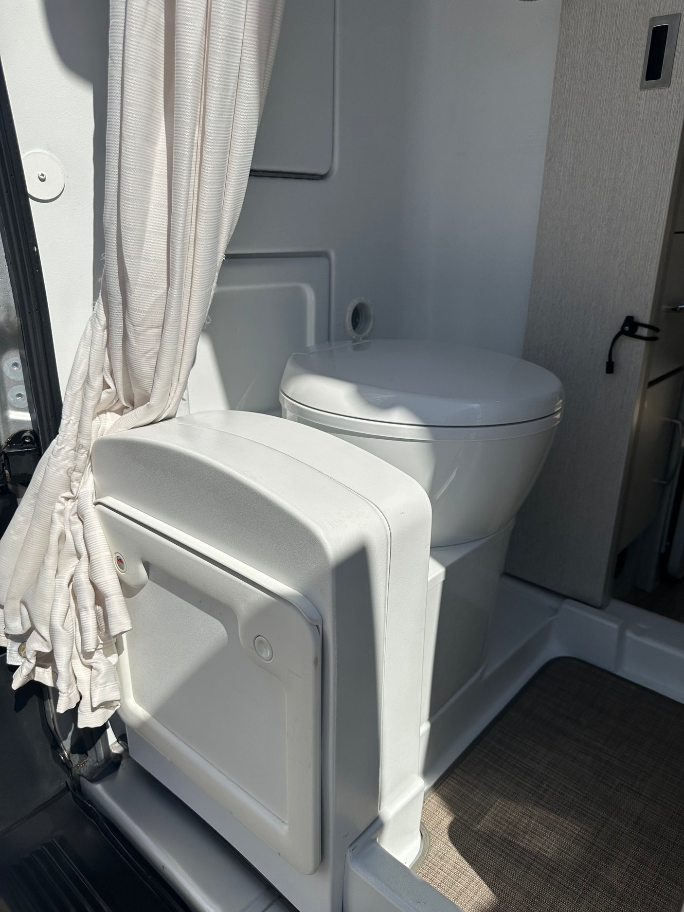 RV rental's compact wet bath features a white toilet, pulled-back shower curtain, and dark floor mat.