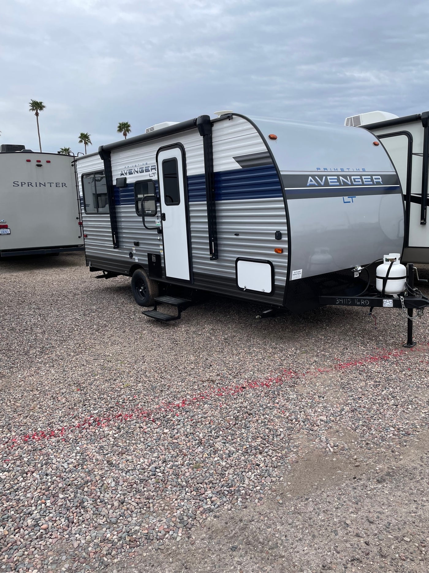 A modern gray and blue 'Avenger LT' travel trailer, perfect for RV rental adventures, parked on a gravel lot. — photo 2