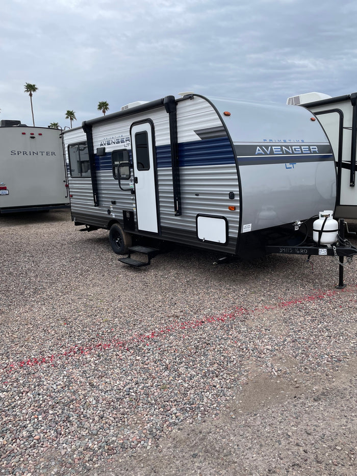 A modern gray and blue 'Avenger LT' travel trailer, perfect for RV rental adventures, parked on a gravel lot.