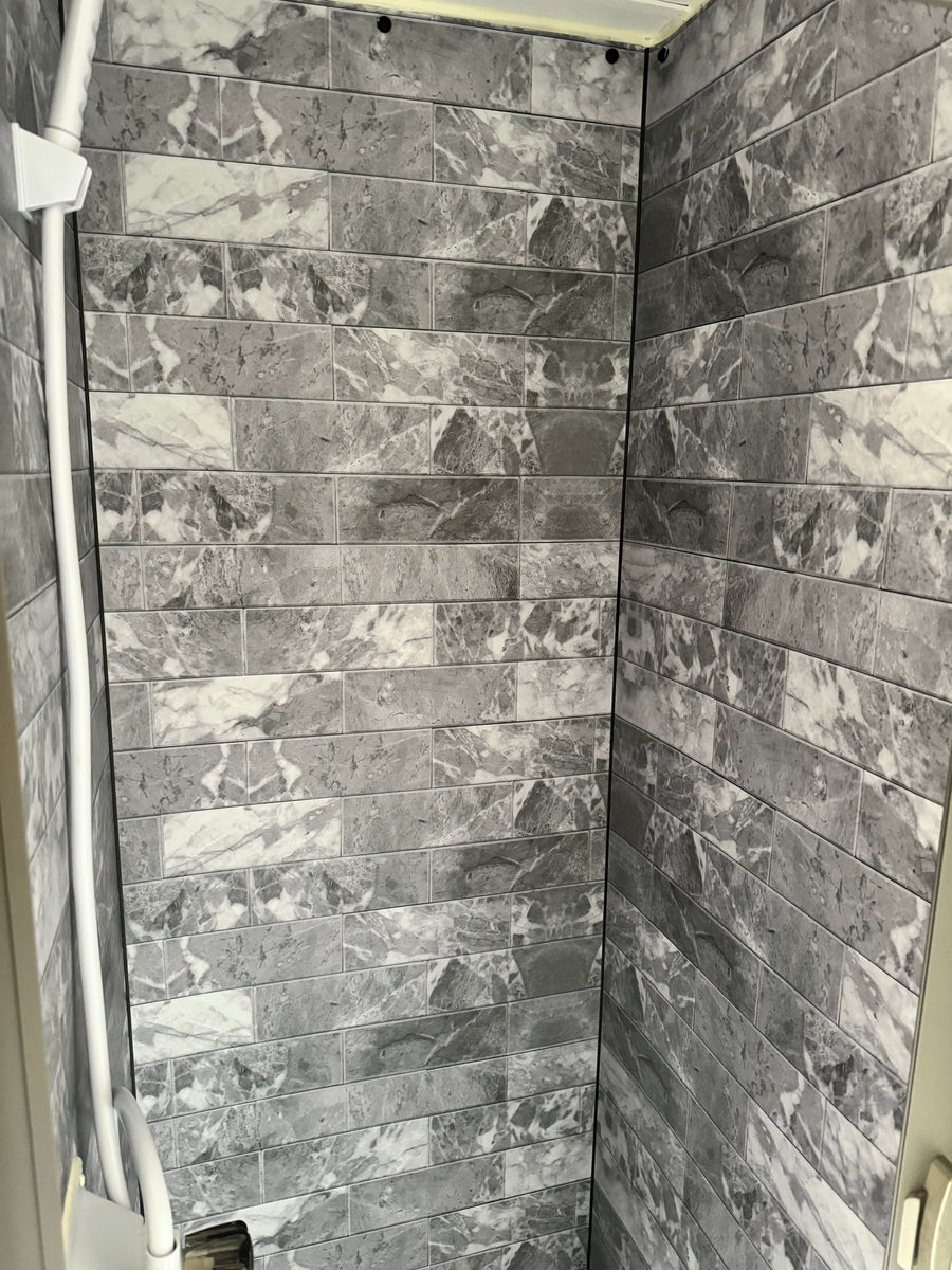 Modern grey & white marble-look tiled shower interior in an RV rental, featuring a white shower rail.