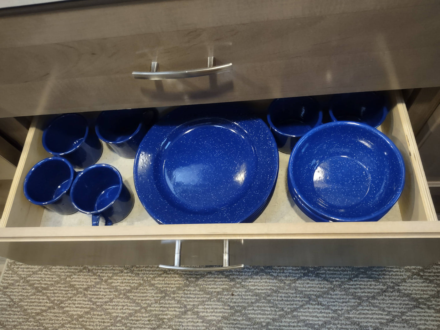 Blue speckled enamel camping dishes (mugs, plates, bowls) in an RV rental kitchen drawer.