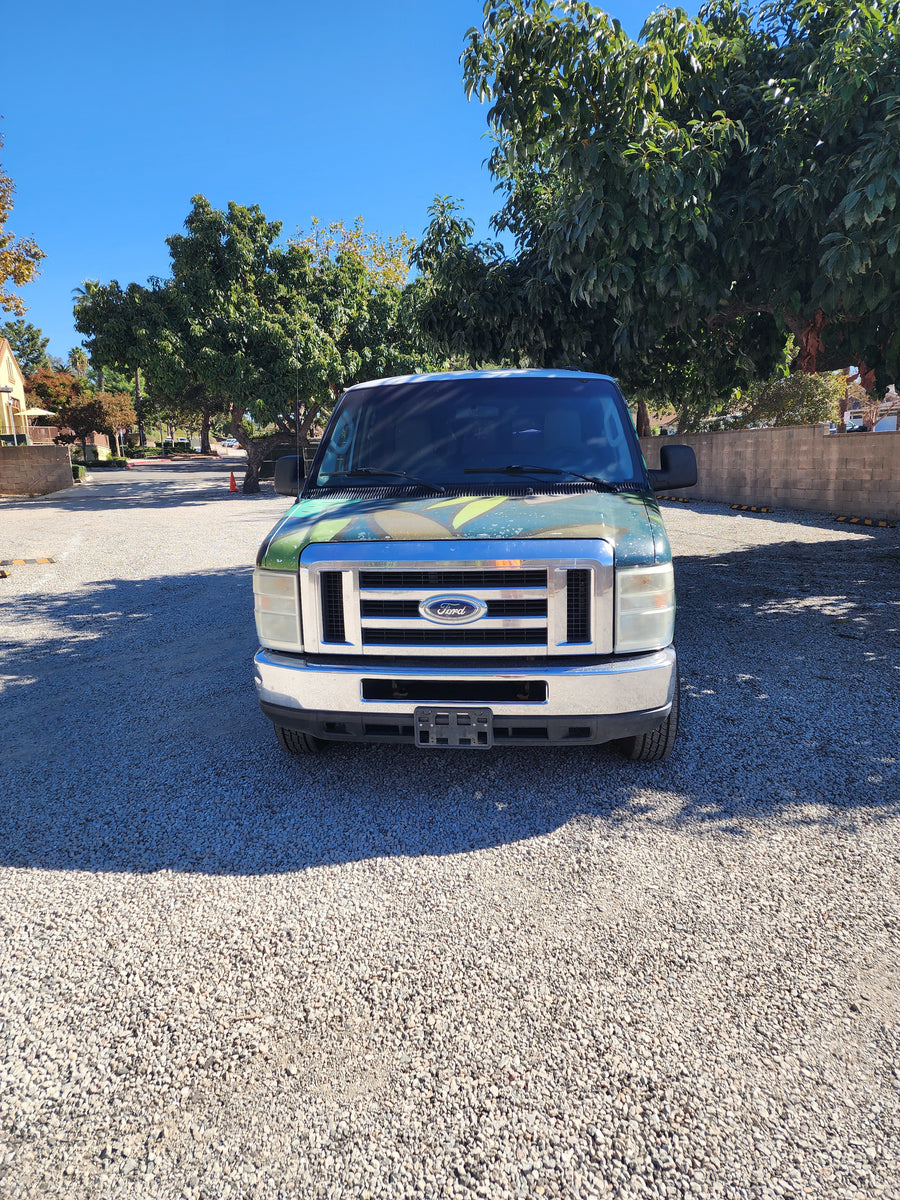Front view of a green Ford van, excellent for RV rental, parked on gravel under a sunny blue sky.