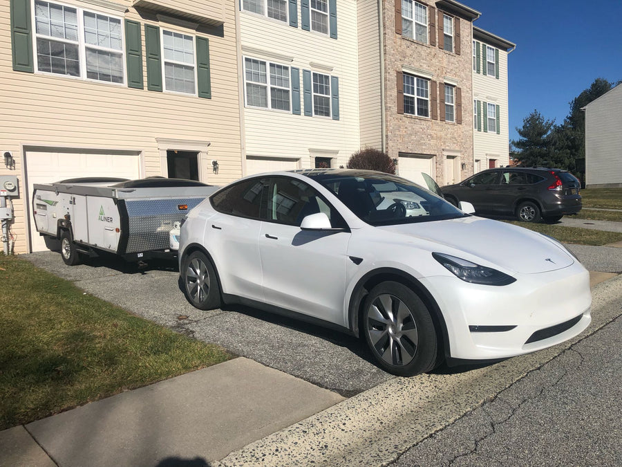 highlighting modern EV towing.|A white A-frame **rv rental** camper is hitched to a Tesla