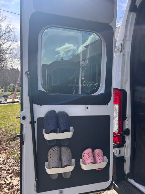 RV rental storage: Pink, blue, and grey clogs secured on a door panel. Efficient shoe organization for camper travel.