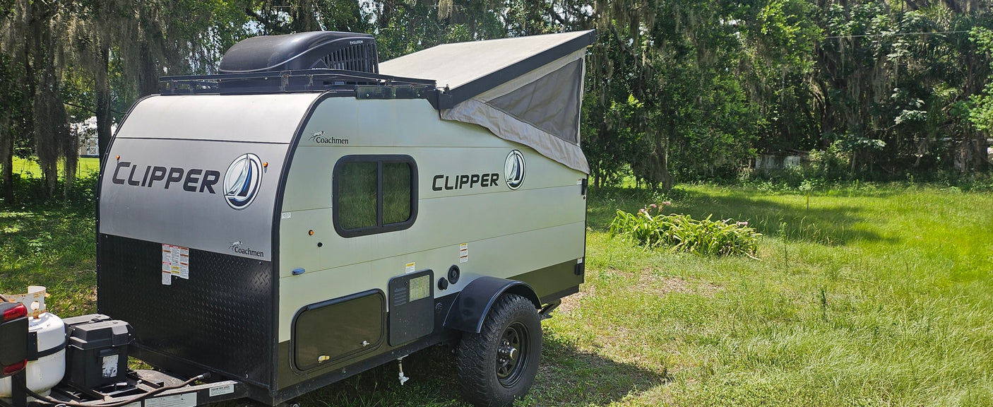 A compact Coachmen Clipper pop-top travel trailer, ready for your rv rental adventure, parked in a green, wooded area.