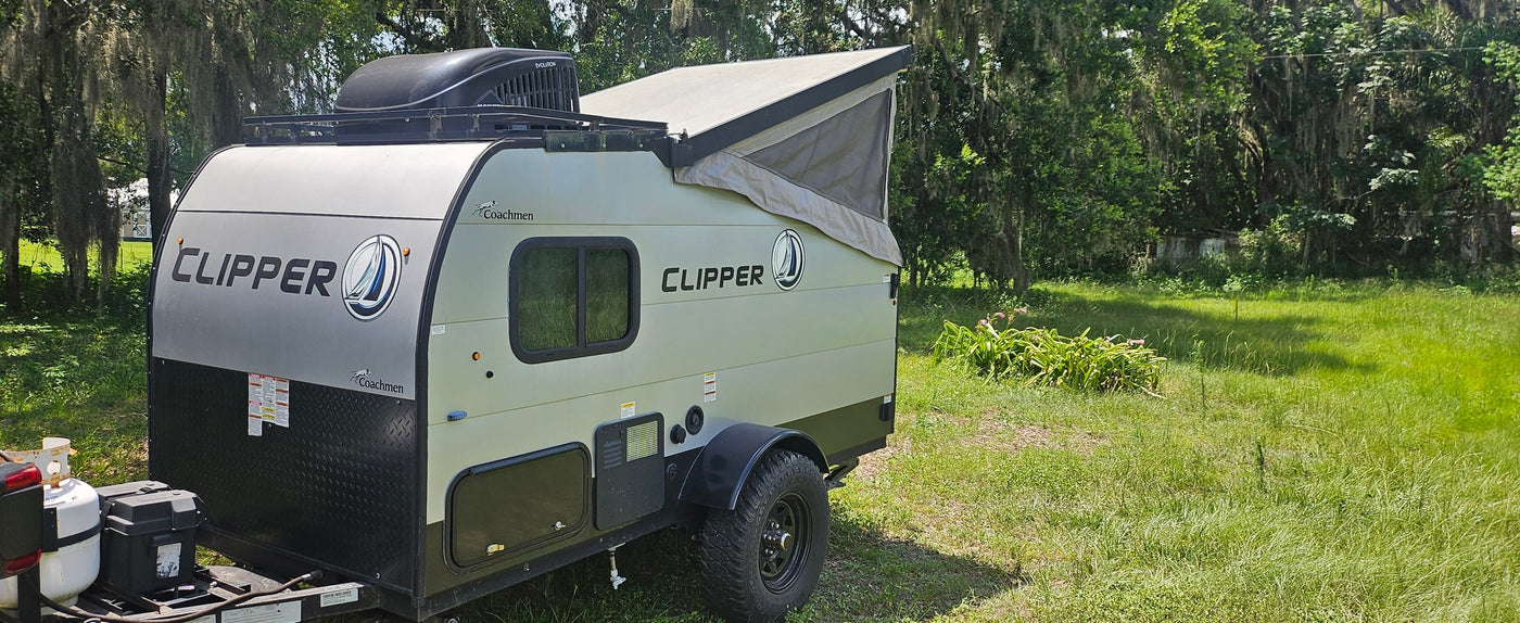 A compact Coachmen Clipper pop-top travel trailer, ready for your rv rental adventure, parked in a green, wooded area. — photo 3