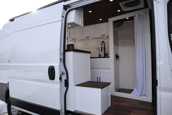 White camper van interior for RV rental. Features a modern kitchen, compact shower, and smart storage solutions.
