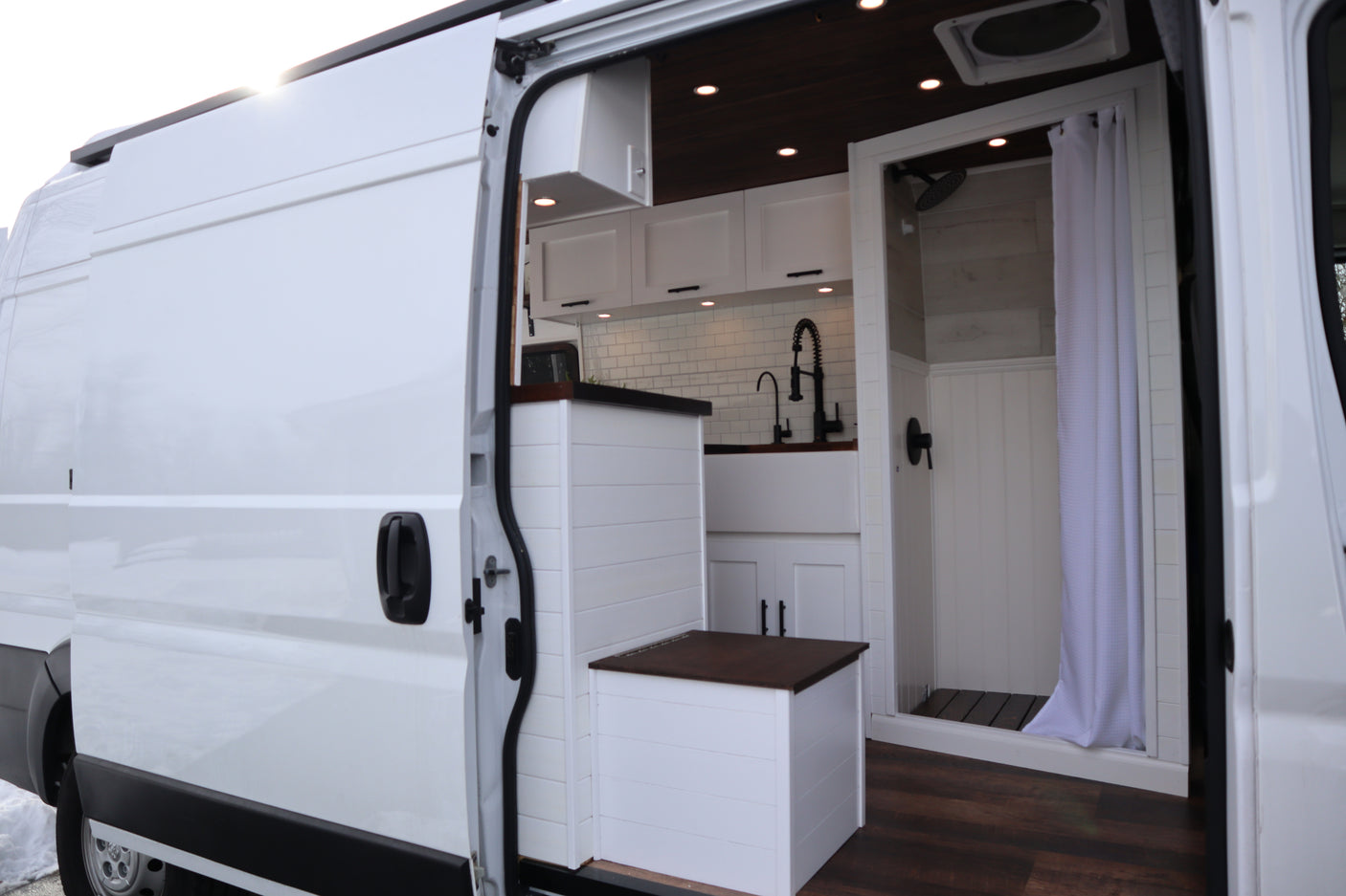 White camper van interior for RV rental. Features a modern kitchen, compact shower, and smart storage solutions.