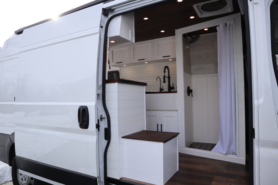 White camper van interior for RV rental. Features a modern kitchen, compact shower, and smart storage solutions.