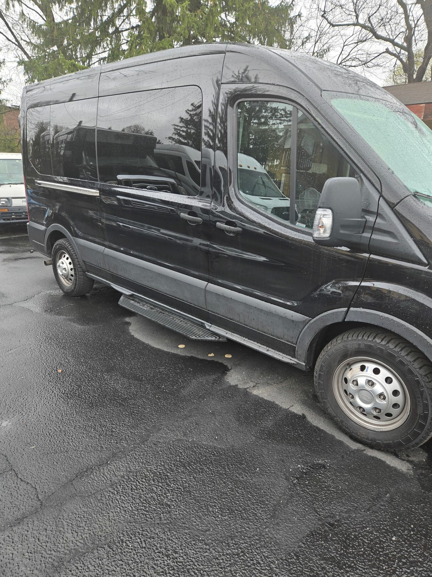 This black passenger van, a versatile RV rental option, is shown parked on wet pavement after rain.