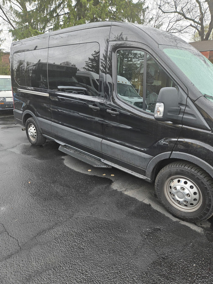 This black passenger van, a versatile RV rental option, is shown parked on wet pavement after rain.