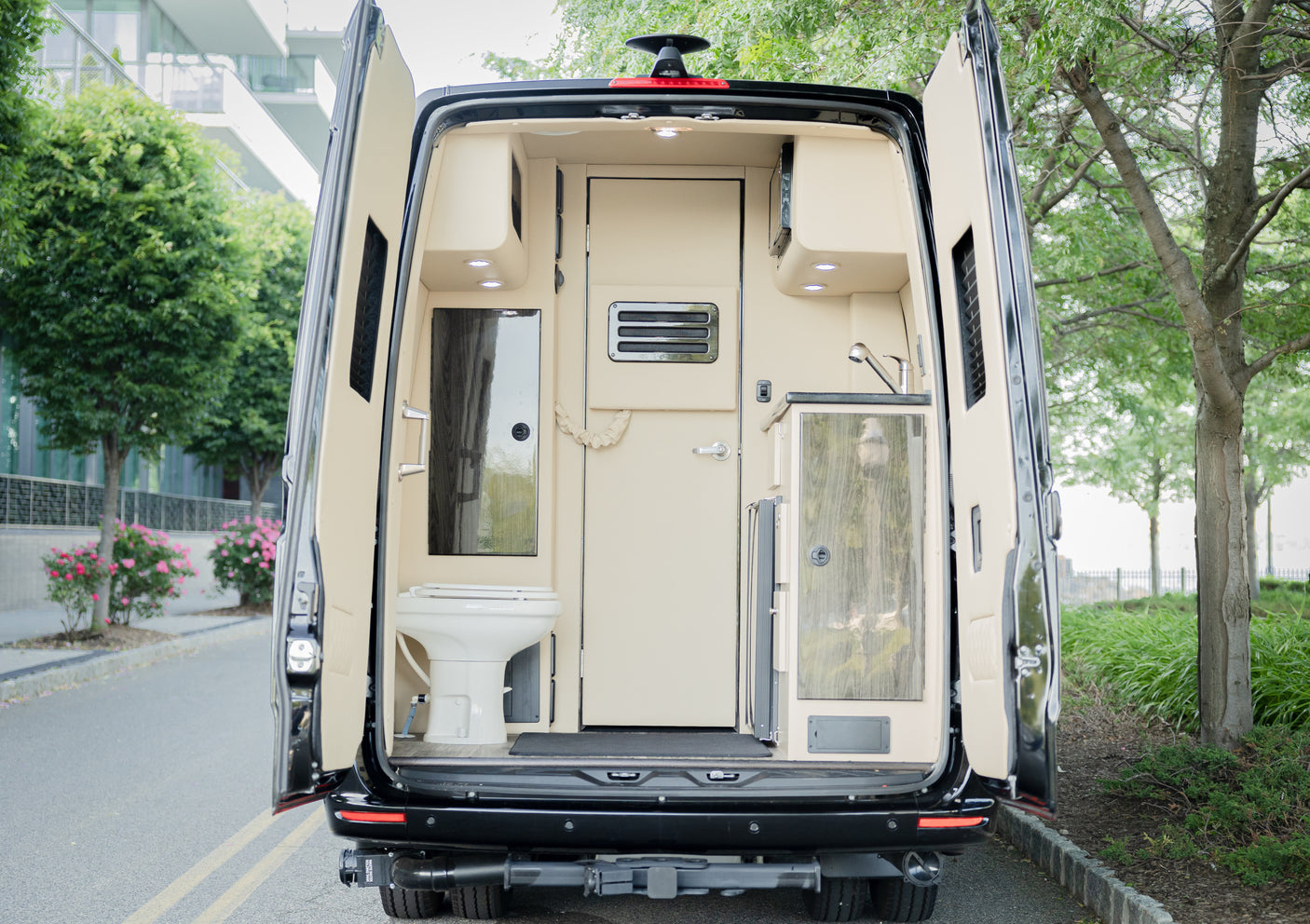 Rear view of an RV rental camper van with open doors, revealing a compact interior with a toilet, sink, and kitchen.