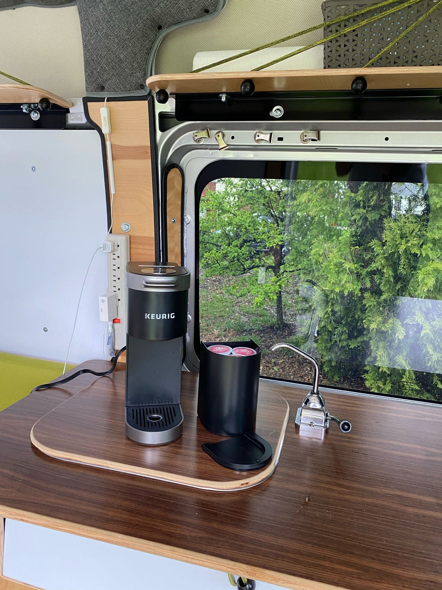 Compact coffee station in an RV rental, featuring a Keurig on a wooden counter with a view of trees. Perfect for mobile living.