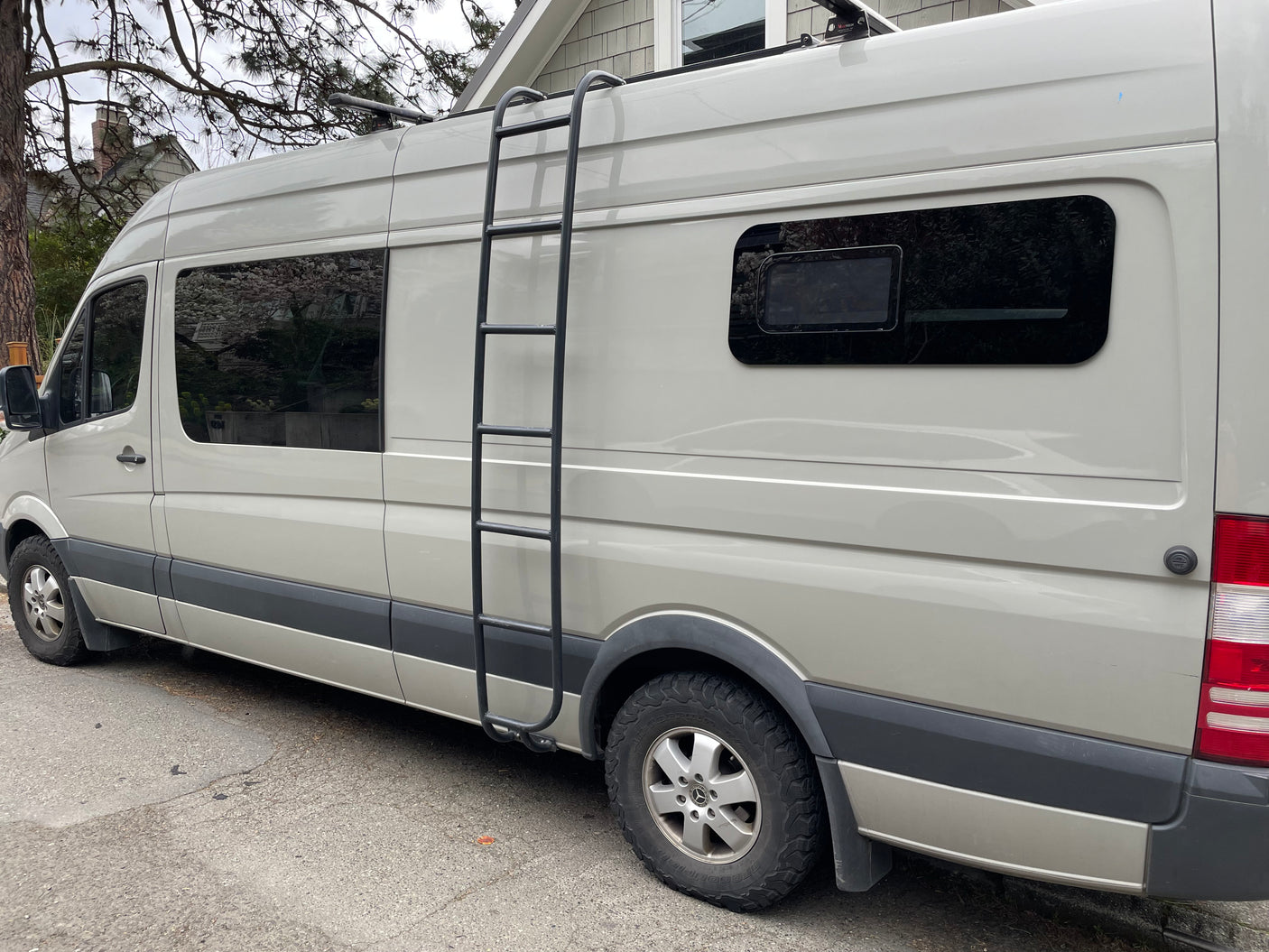 Light-colored Mercedes-Benz Sprinter camper van, likely an RV rental, with a side ladder and roof racks. Ready for adventure.