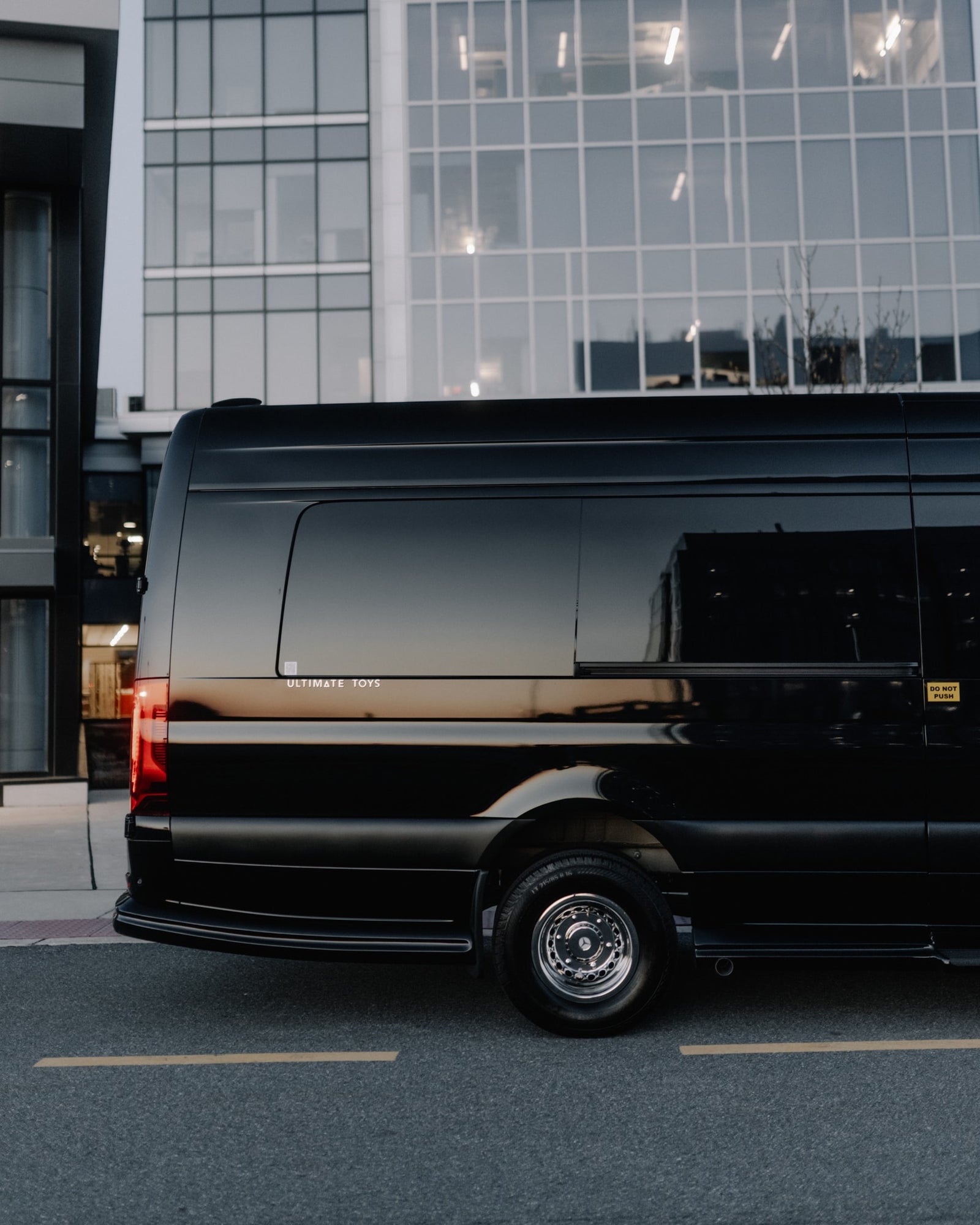 A sleek black luxury van, branded 'Ultimate Toys', by modern buildings. Perfect for premium RV rental.
