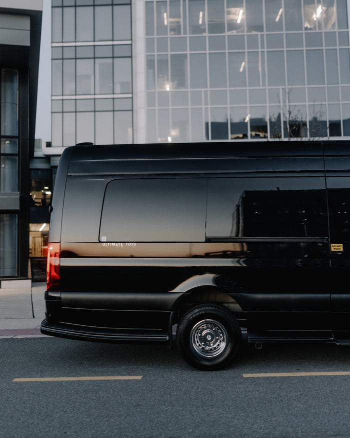 A sleek black luxury van, branded 'Ultimate Toys', by modern buildings. Perfect for premium RV rental.
