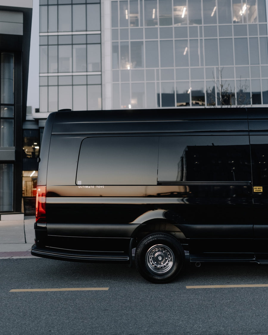 A sleek black luxury van, branded 'Ultimate Toys', by modern buildings. Perfect for premium RV rental.