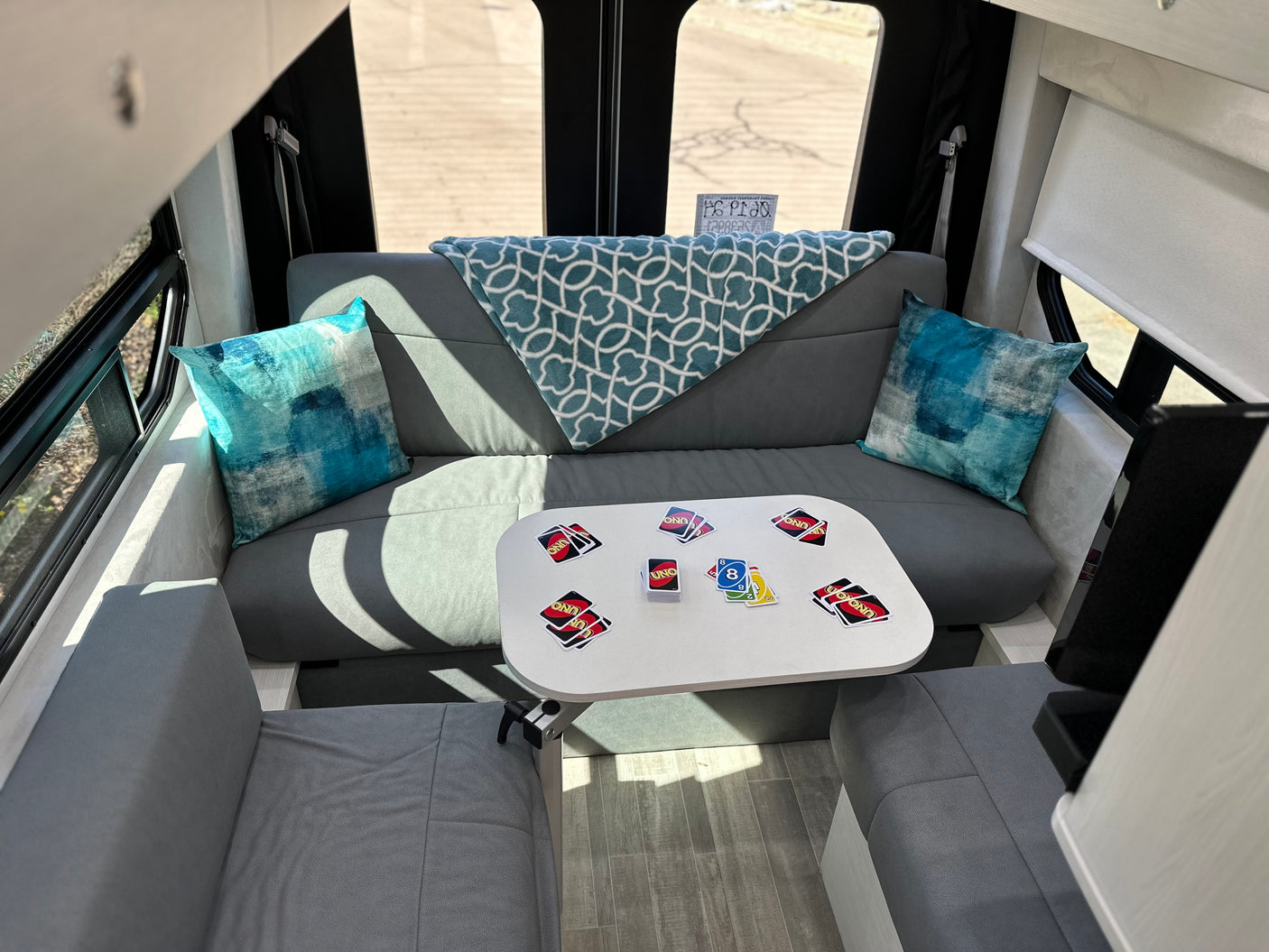 Cozy RV rental interior showing a U-shaped lounge with a table, UNO game cards, and blue pillows.