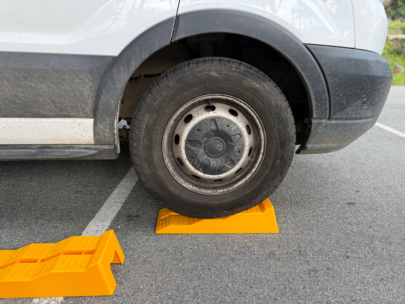 RV rental van parked with its dirty wheel on yellow leveling blocks, with another block nearby, ensuring a stable campsite setup.