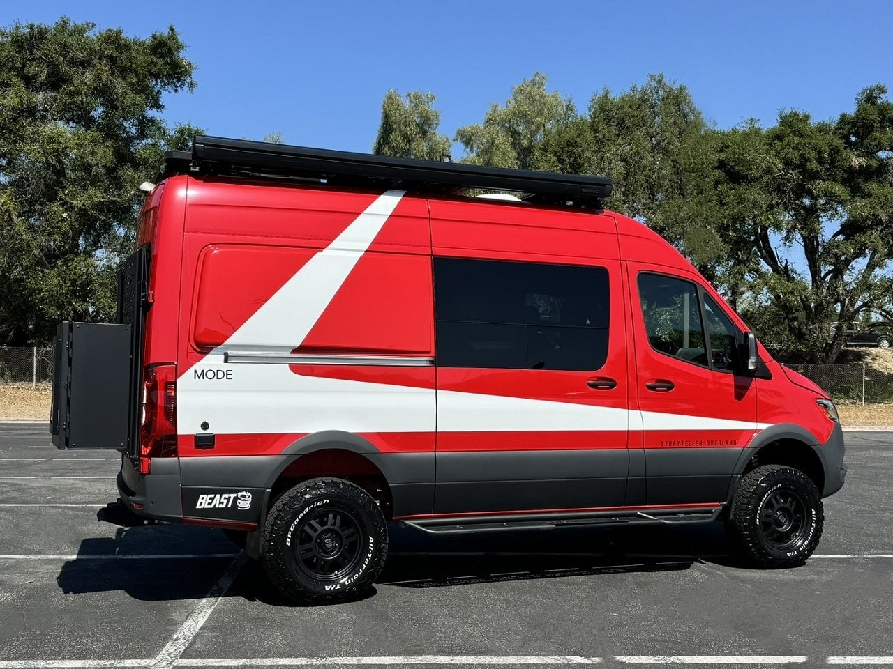 Vibrant red & white Storyteller Overland camper van ready for your next rv rental adventure. Parked outdoors with all-terrain tires.