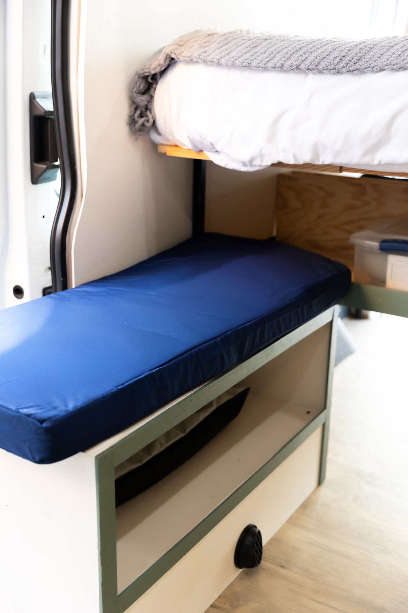 Cozy rv rental interior with bunk beds and storage, featuring a blue cushion bench and white top bunk for van life adventures.