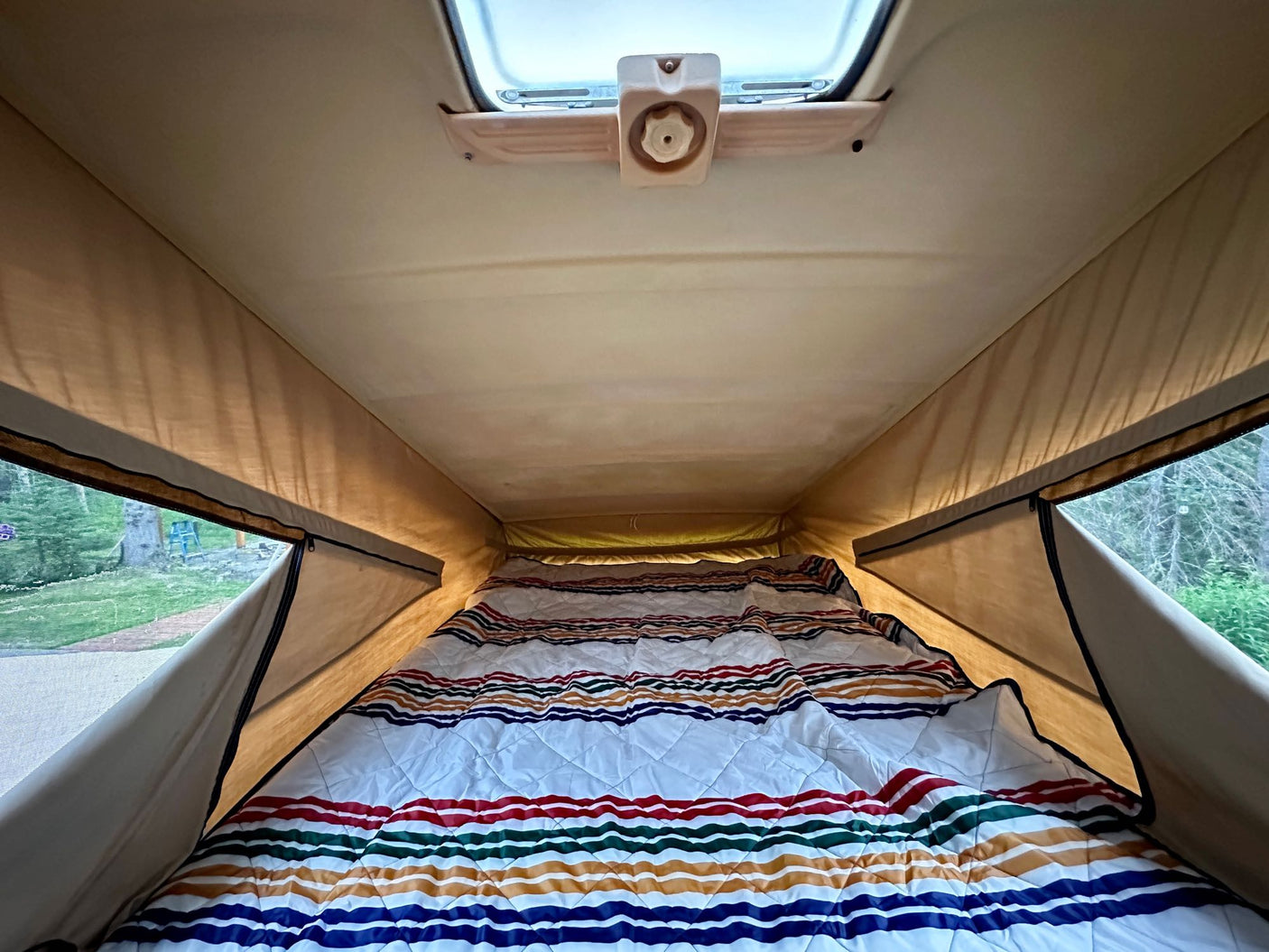 Explore nature's beauty from this cozy pop-top rv rental bed with a vibrant striped comforter, visible through the windows.