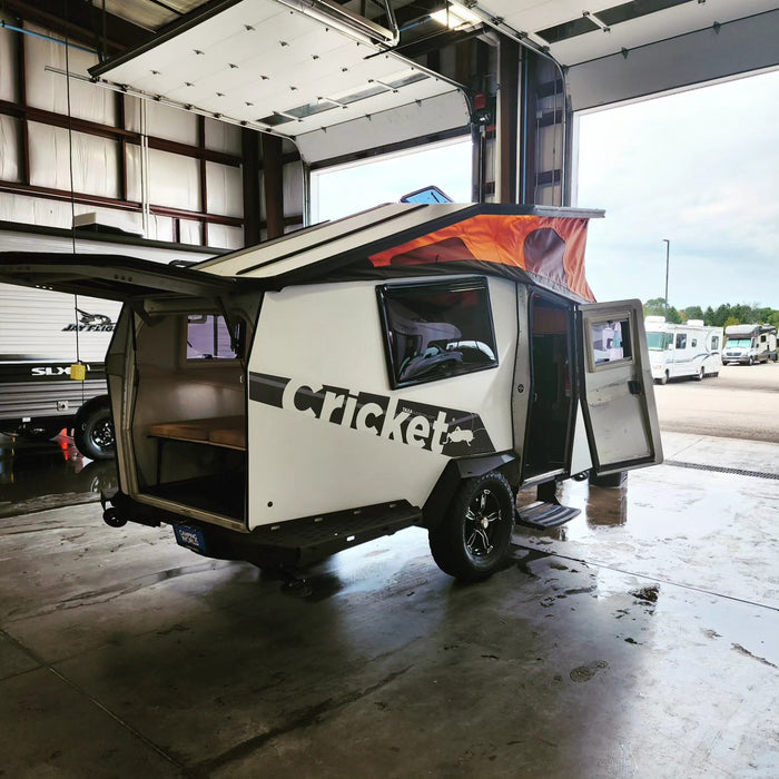 White & black Cricket travel trailer with orange pop-top roof, ideal for rv rental, in a garage bay after a wash.