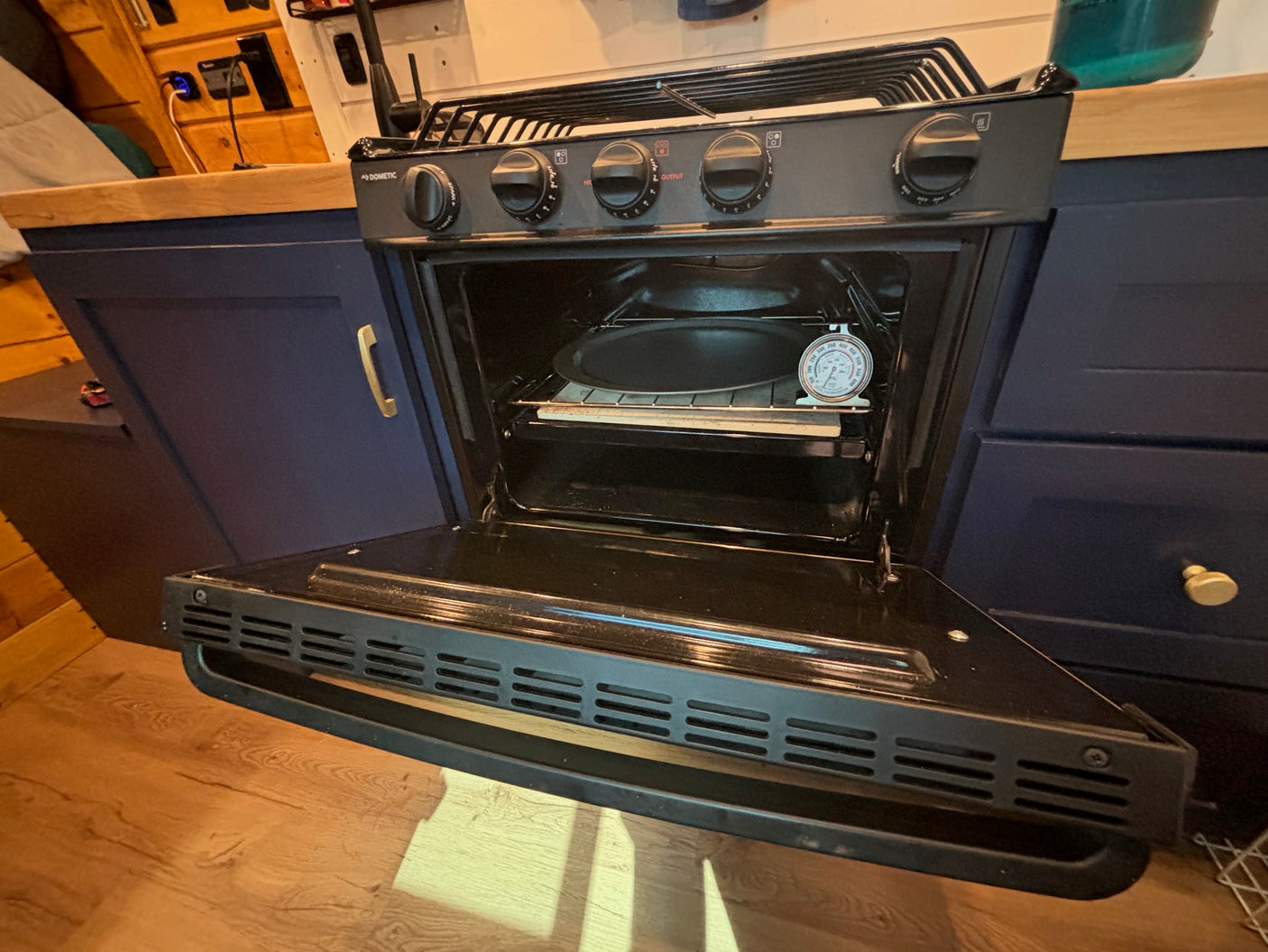 RV rental kitchen: Open Dometic oven with pan and thermometer, showing compact setup for mobile cooking.