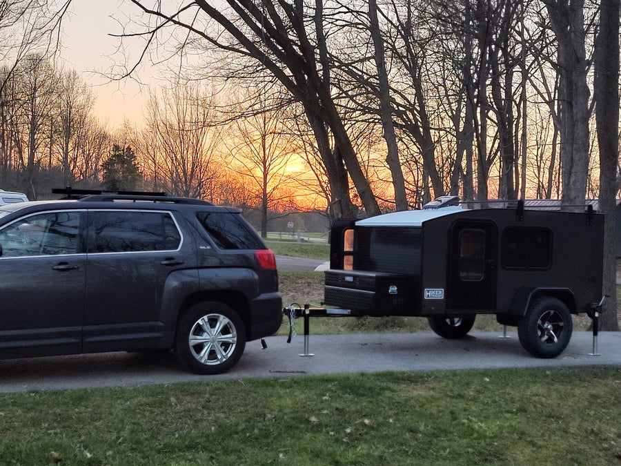 SUV towing a black Hiker camping trailer at sunset. Consider an RV rental for your next outdoor adventure!