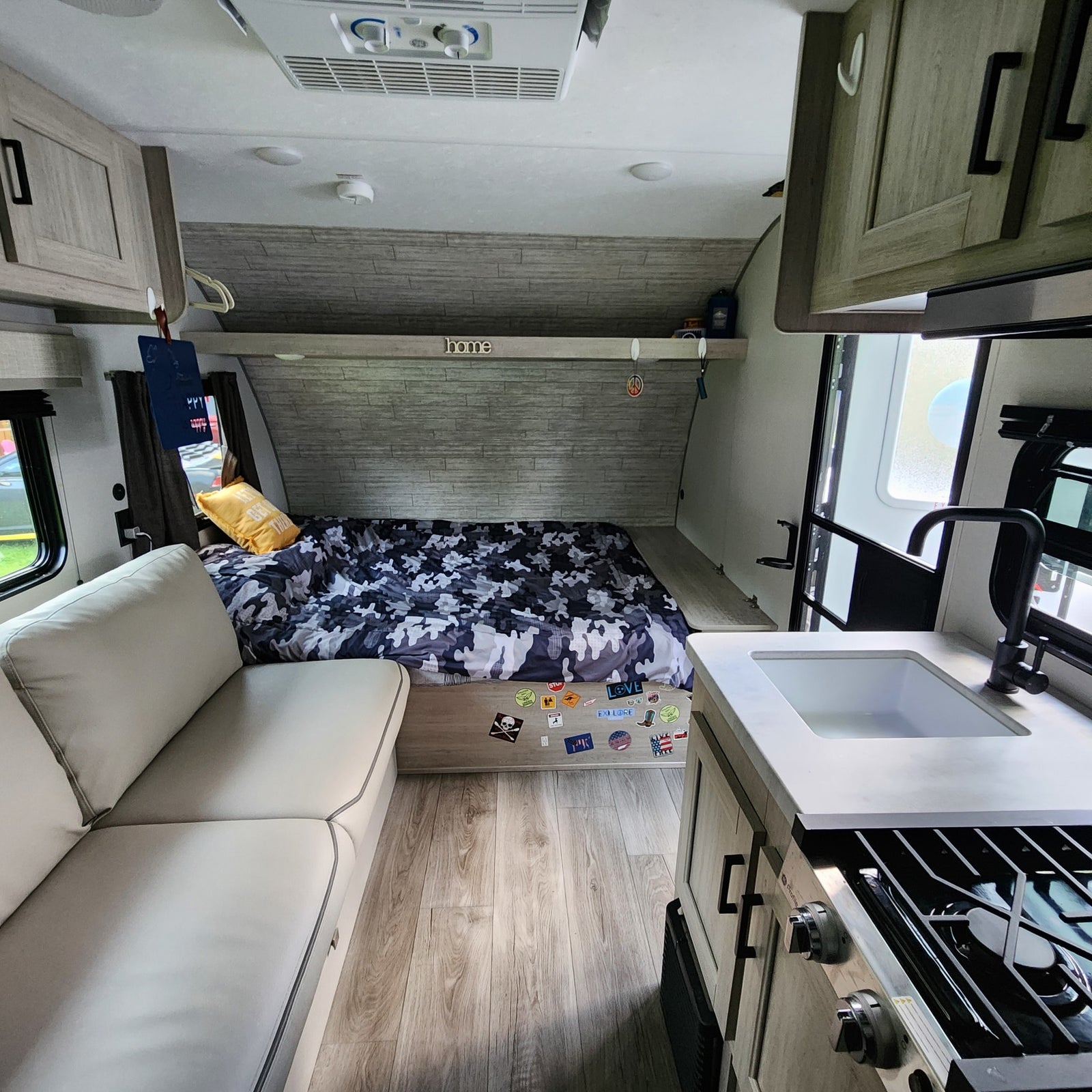 Cozy RV rental interior: camo bed, light sofa, and compact kitchen, ready for adventure.