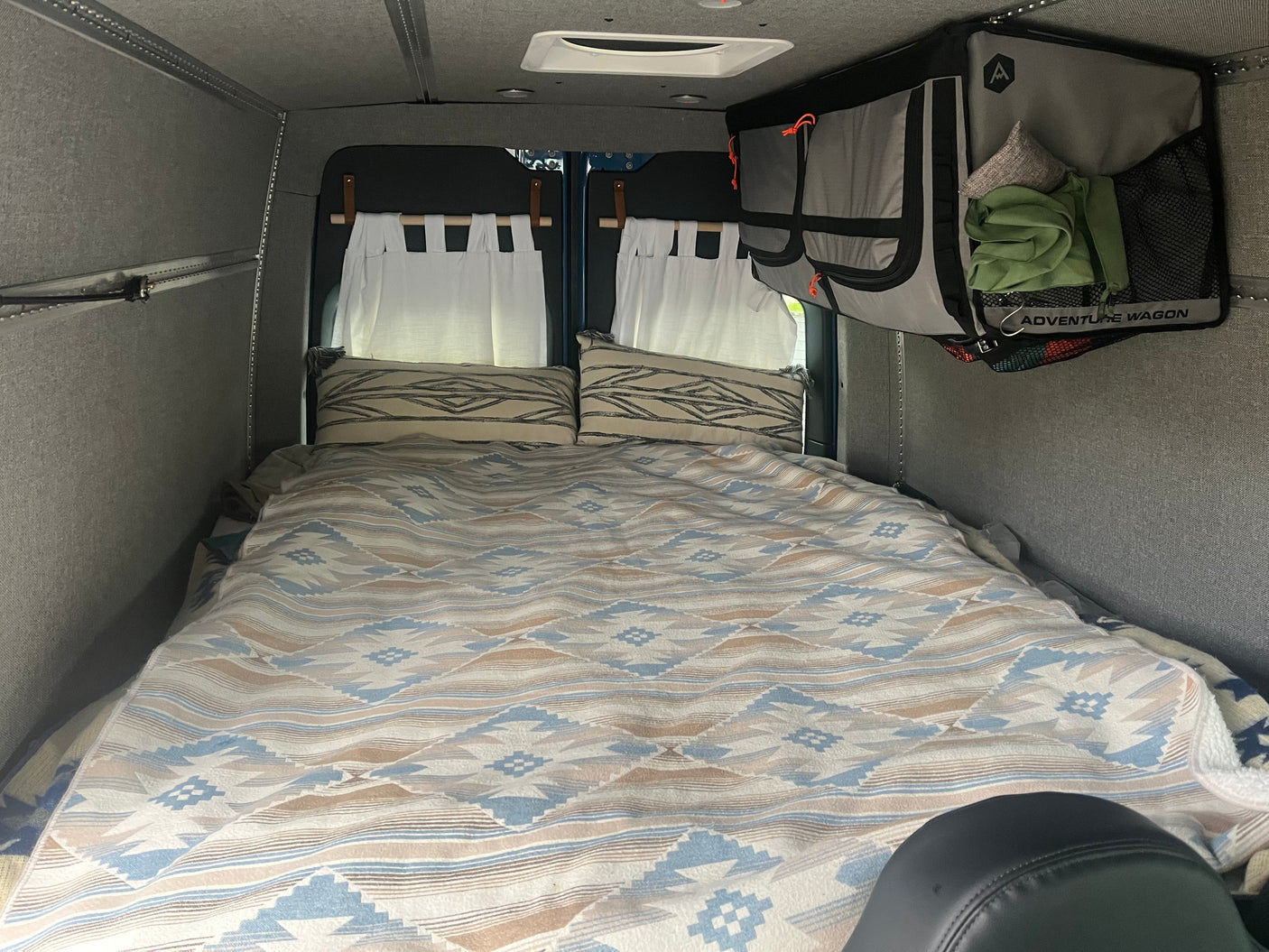 Cozy RV rental sleeping area features patterned bedding, pillows, and hanging storage.