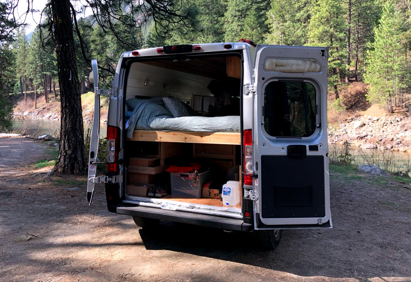 Discover adventure with an rv rental. This camper van offers a cozy bed & storage by a peaceful river in nature.