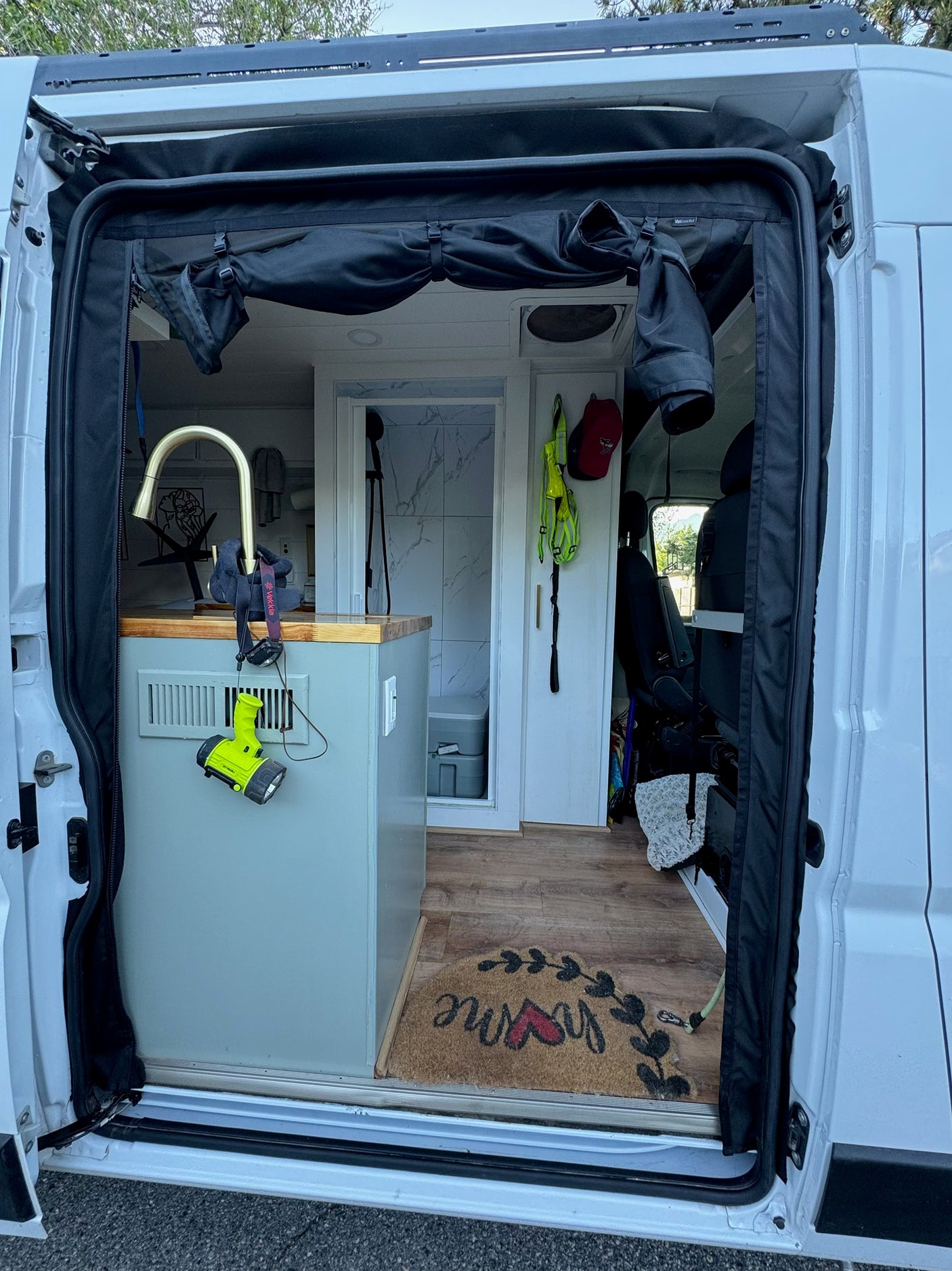 An open rv rental side door reveals a custom camper van interior with a kitchen, bath, and welcoming "home" mat.
