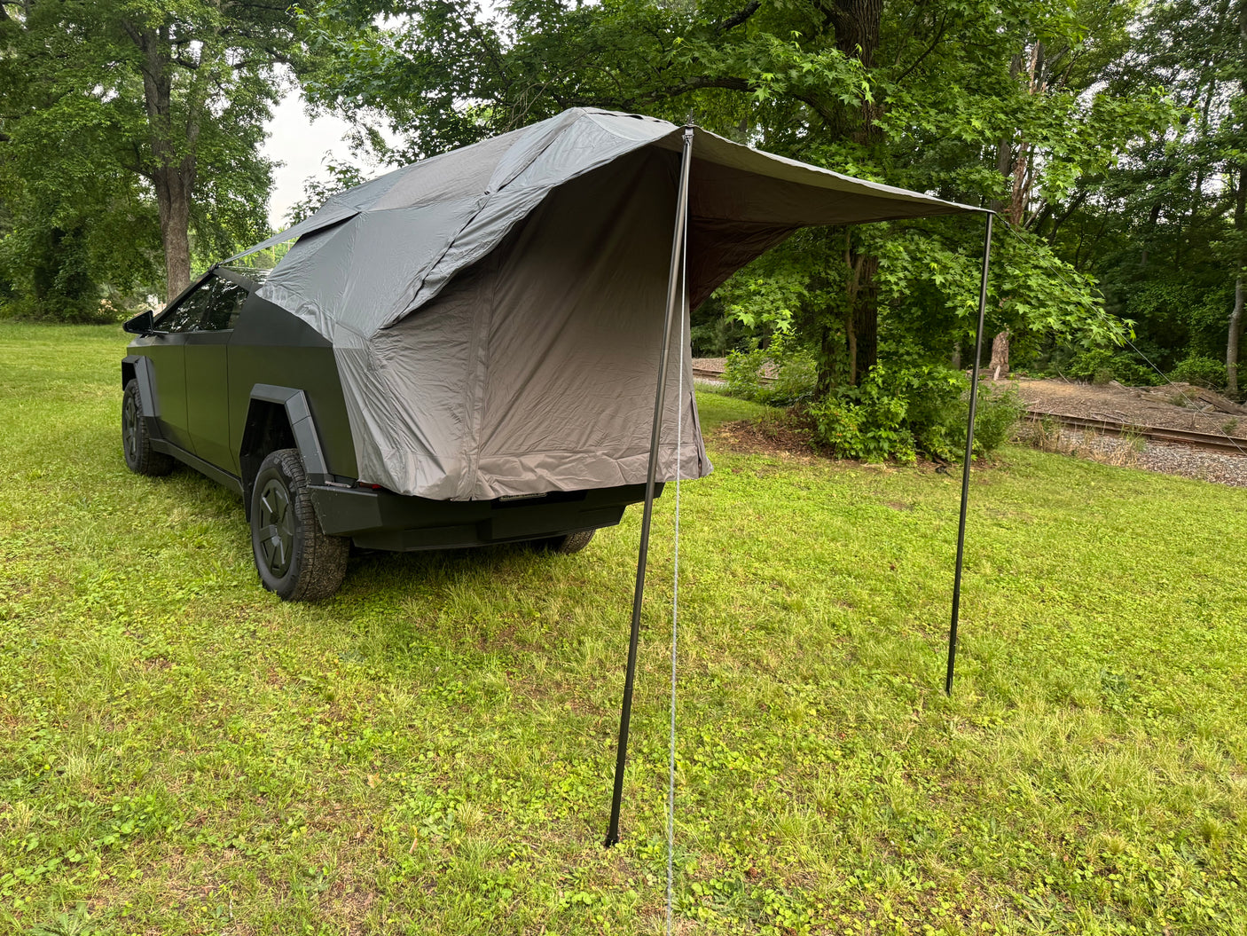 Dark grey Tesla Cybertruck with an attached rear tent, parked on grass. A unique RV rental option for outdoor adventure.