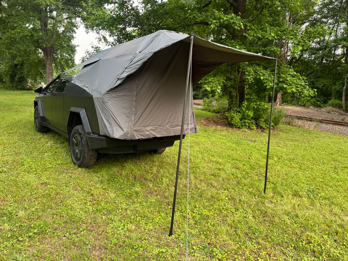 Dark grey Tesla Cybertruck with an attached rear tent, parked on grass. A unique RV rental option for outdoor adventure.