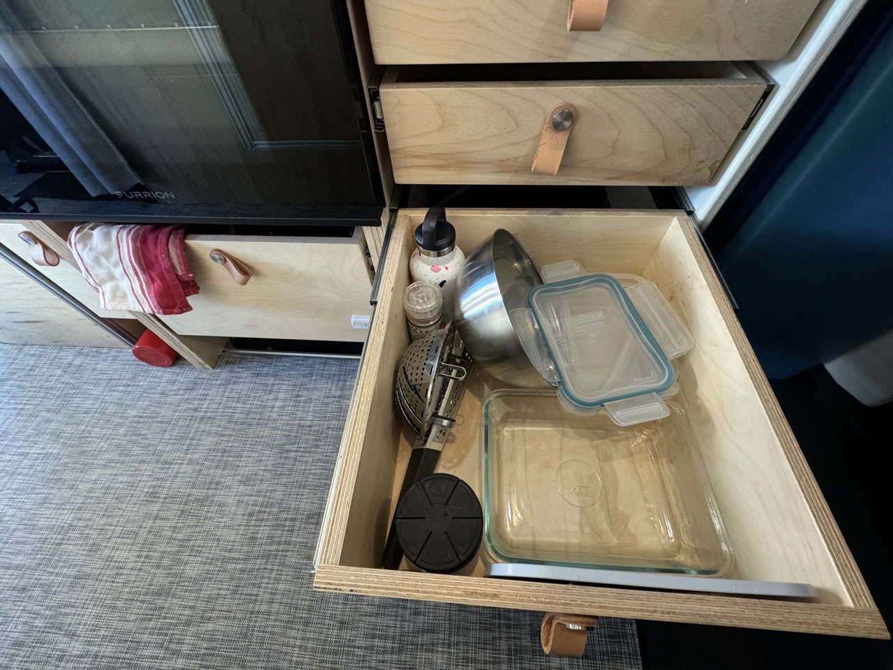 Efficient RV rental kitchen storage with pull-out drawers, showing various cooking essentials and glass containers.