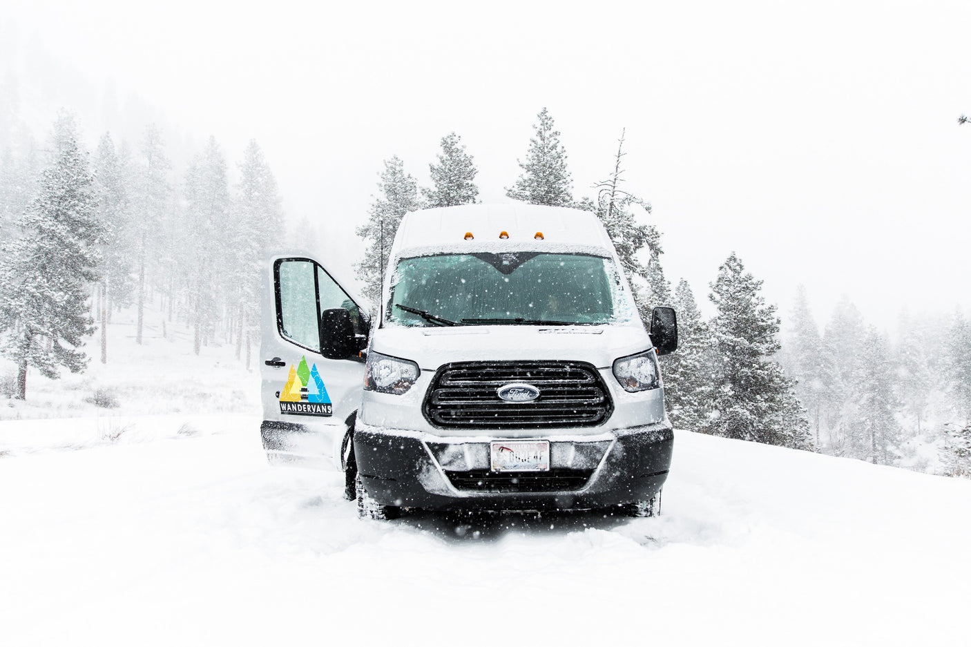 WANDERVANS Ford Transit RV rental van parked in deep snow during a winter storm, driver's door open.