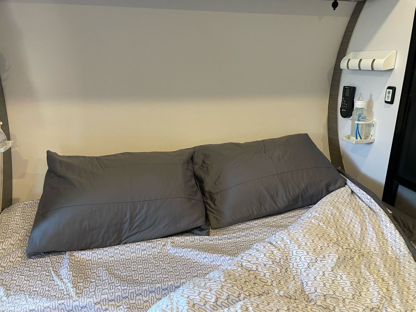 Comfortable RV rental bedroom with patterned bedding, dark pillows, and convenient wall amenities including a baby bottle.