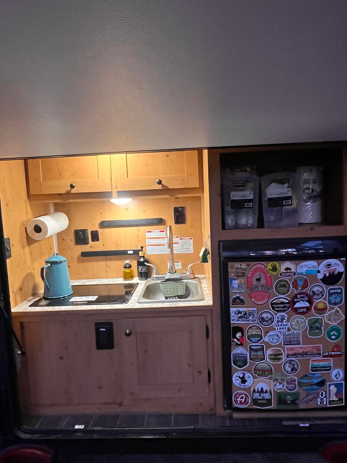 RV rental kitchen: functional space with a sink, stovetop, and a fridge adorned with diverse travel stickers.