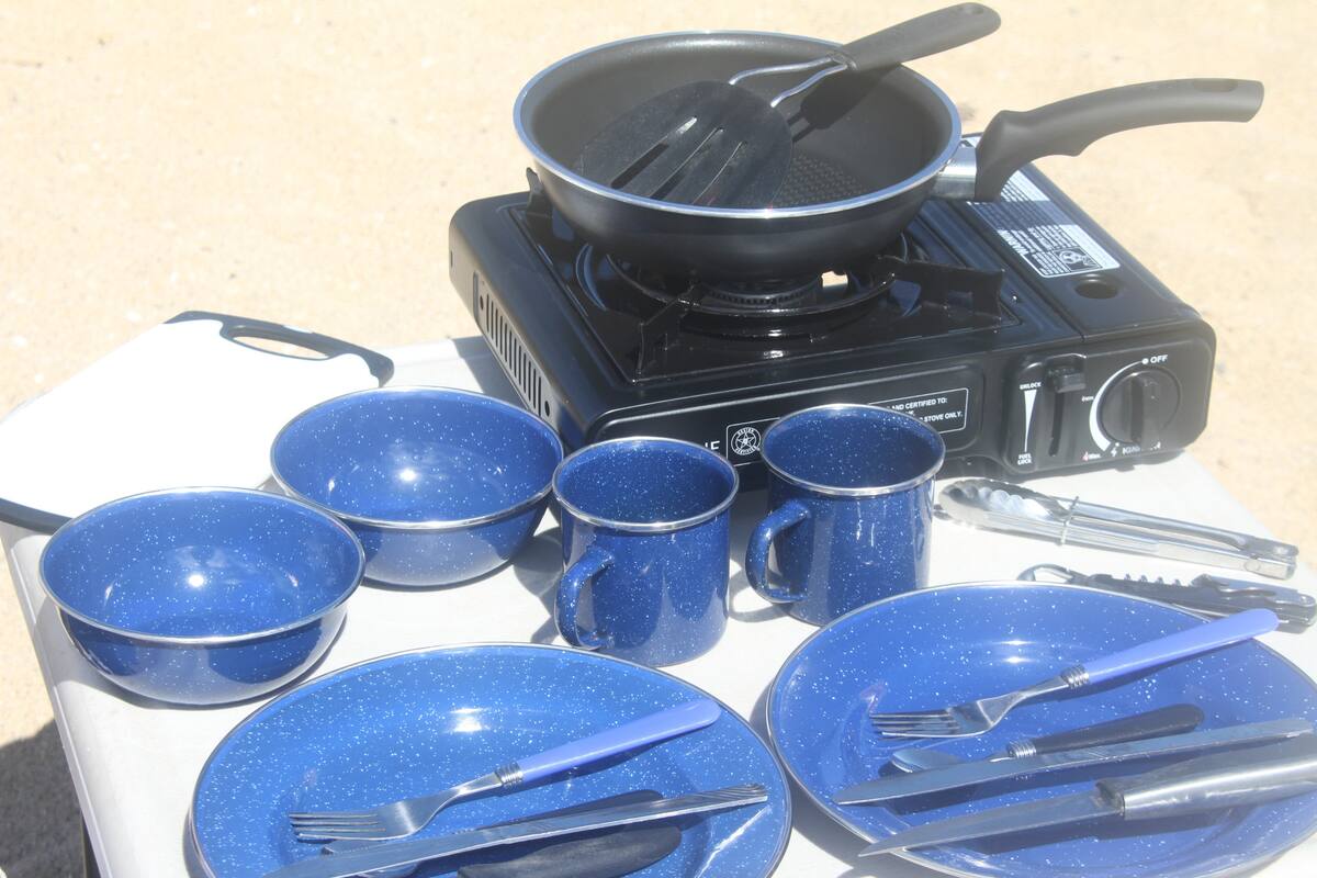 ideal for an RV rental adventure. Features a comfortable bed with plaid bedding and a view of nature.|Essential RV rental camping gear: Portable stove