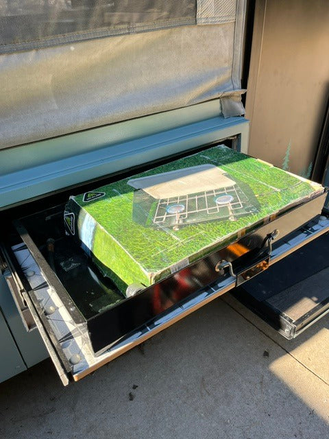 RV rental prep: Slide-out drawer reveals a portable camping stove box, ready for delicious outdoor cooking adventures!