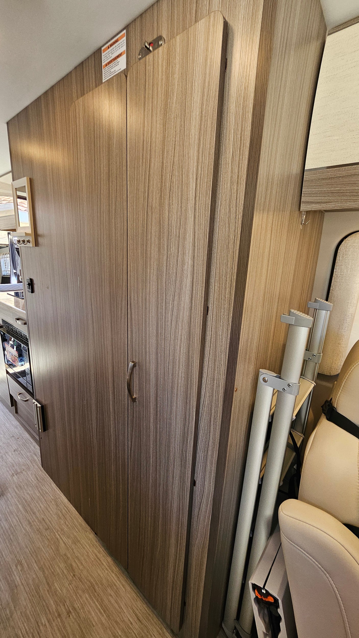 RV rental interior showcasing wood-grain cabinetry, oven, and compact storage for table poles next to the beige passenger seat.
