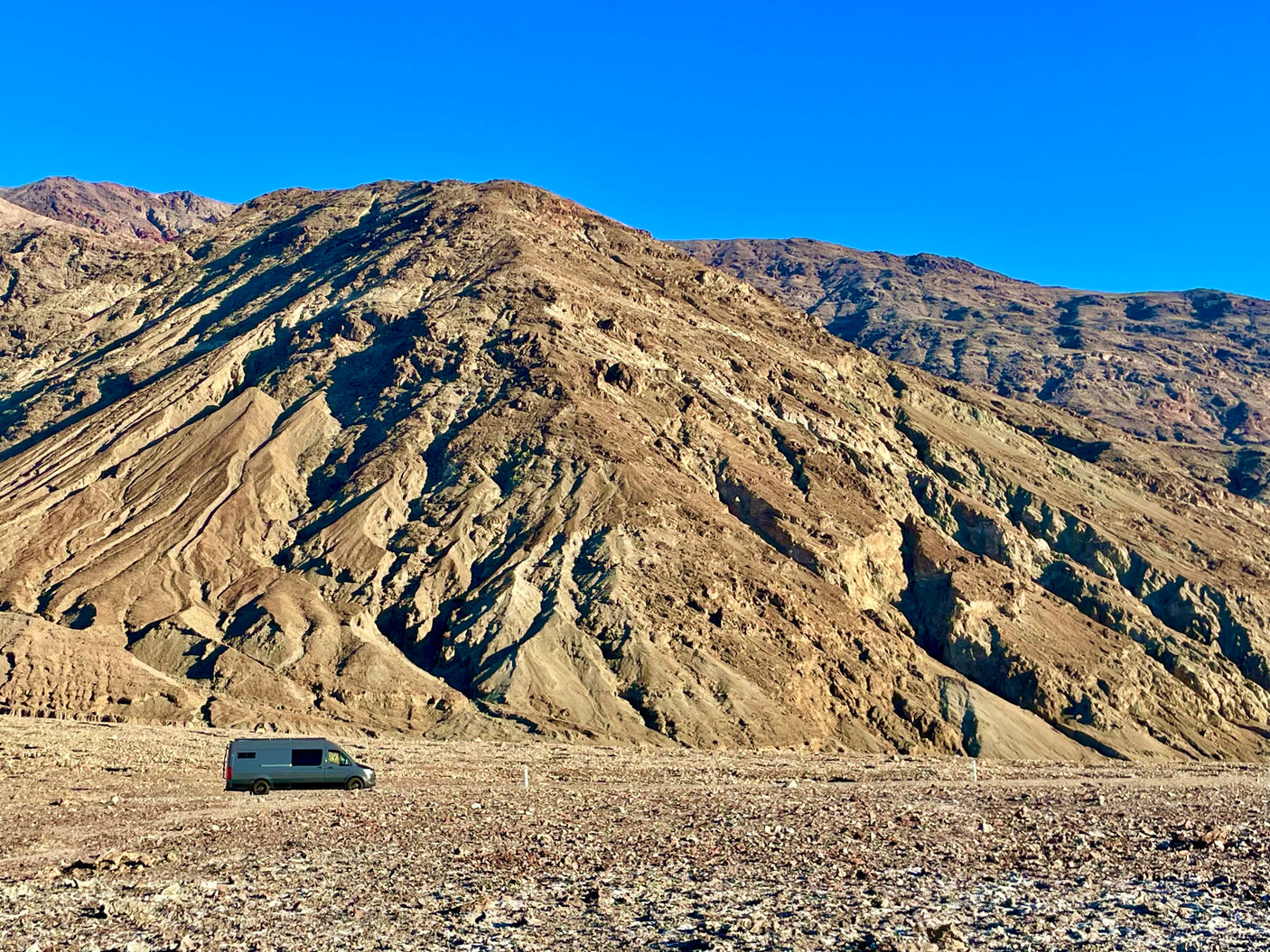 RV rental: A grey camper van on a vast, rocky desert floor under a clear sky, backed by arid mountains.