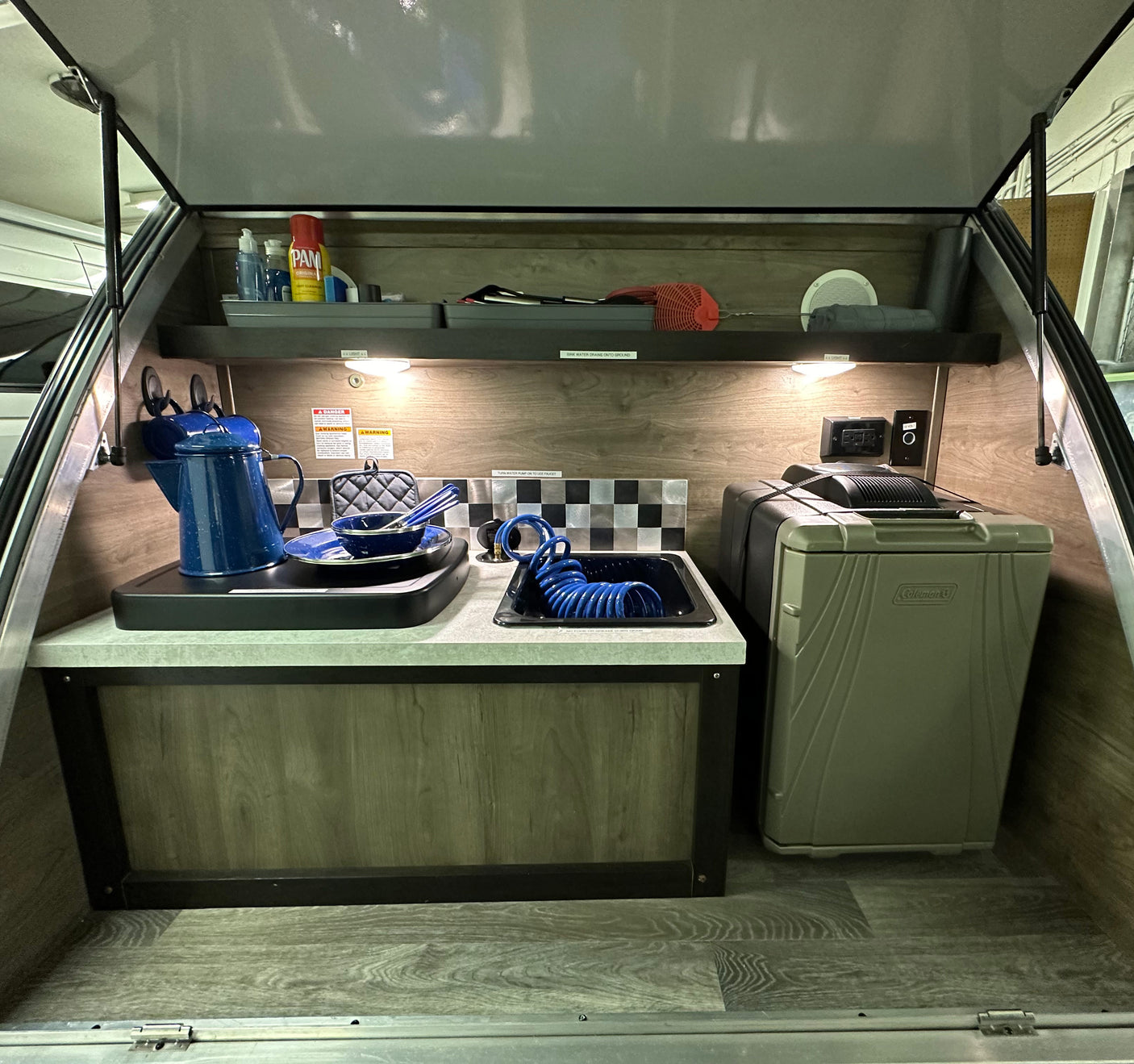 An RV rental's compact outdoor kitchen: sink, cooktop, and Coleman cooler. Ready for camping adventures.