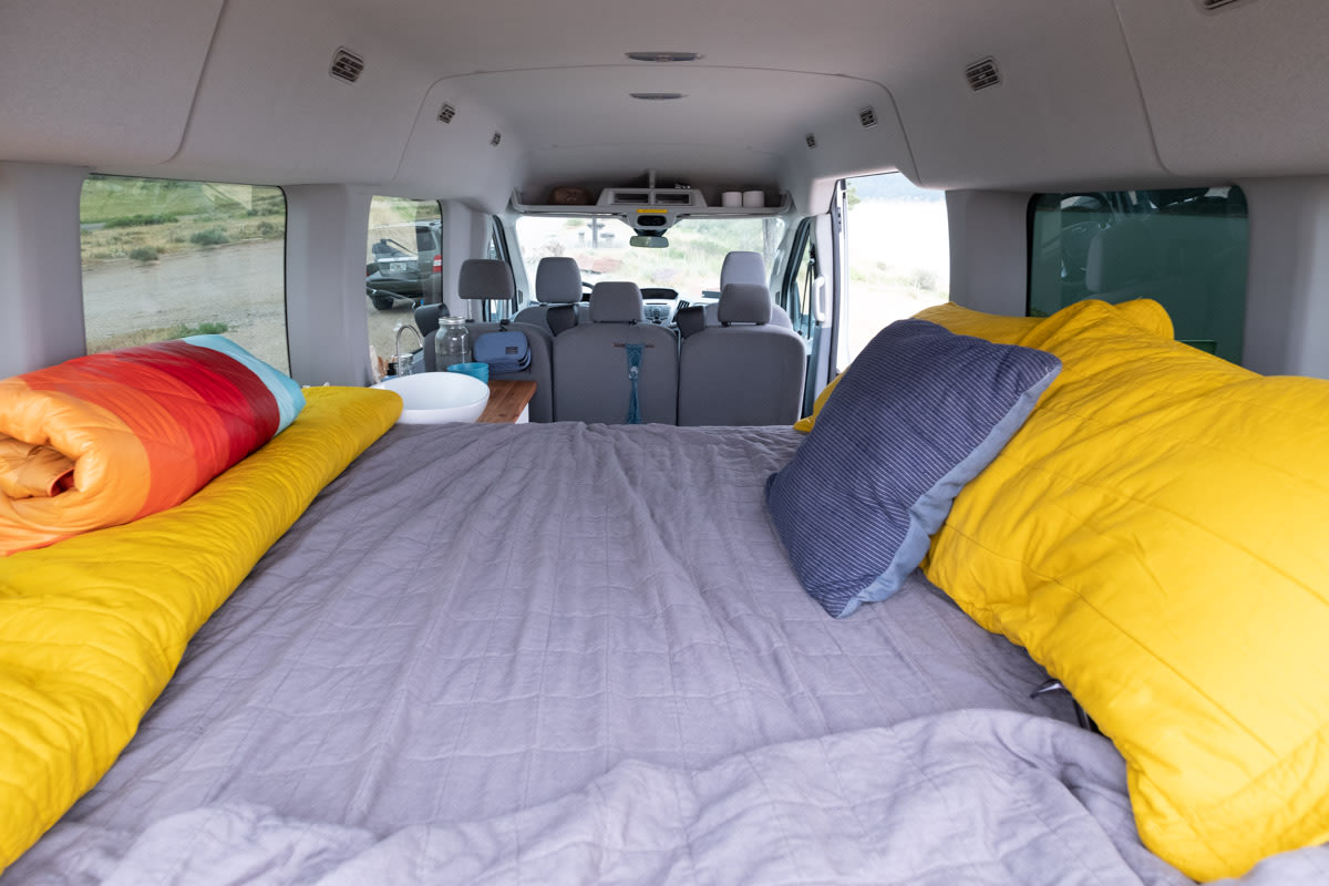 enjoying lake views & conversation.|An RV rental provides a scenic journey. Children look out at a beautiful lake and distant mountains from inside the vehicle.|A child arranges toy cars on a wooden beam next to a parked white RV rental van